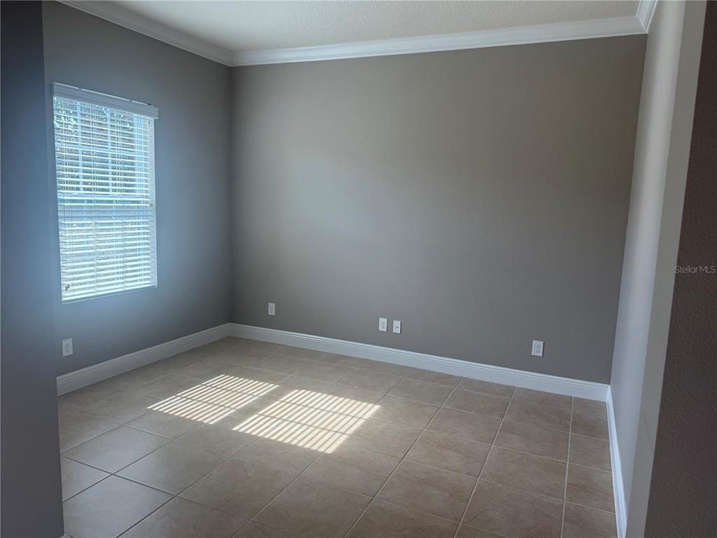 An empty room with grey walls, tile flooring, crown molding, and a single window — 3128 AMALFI DRIVE, ORLANDO, FL