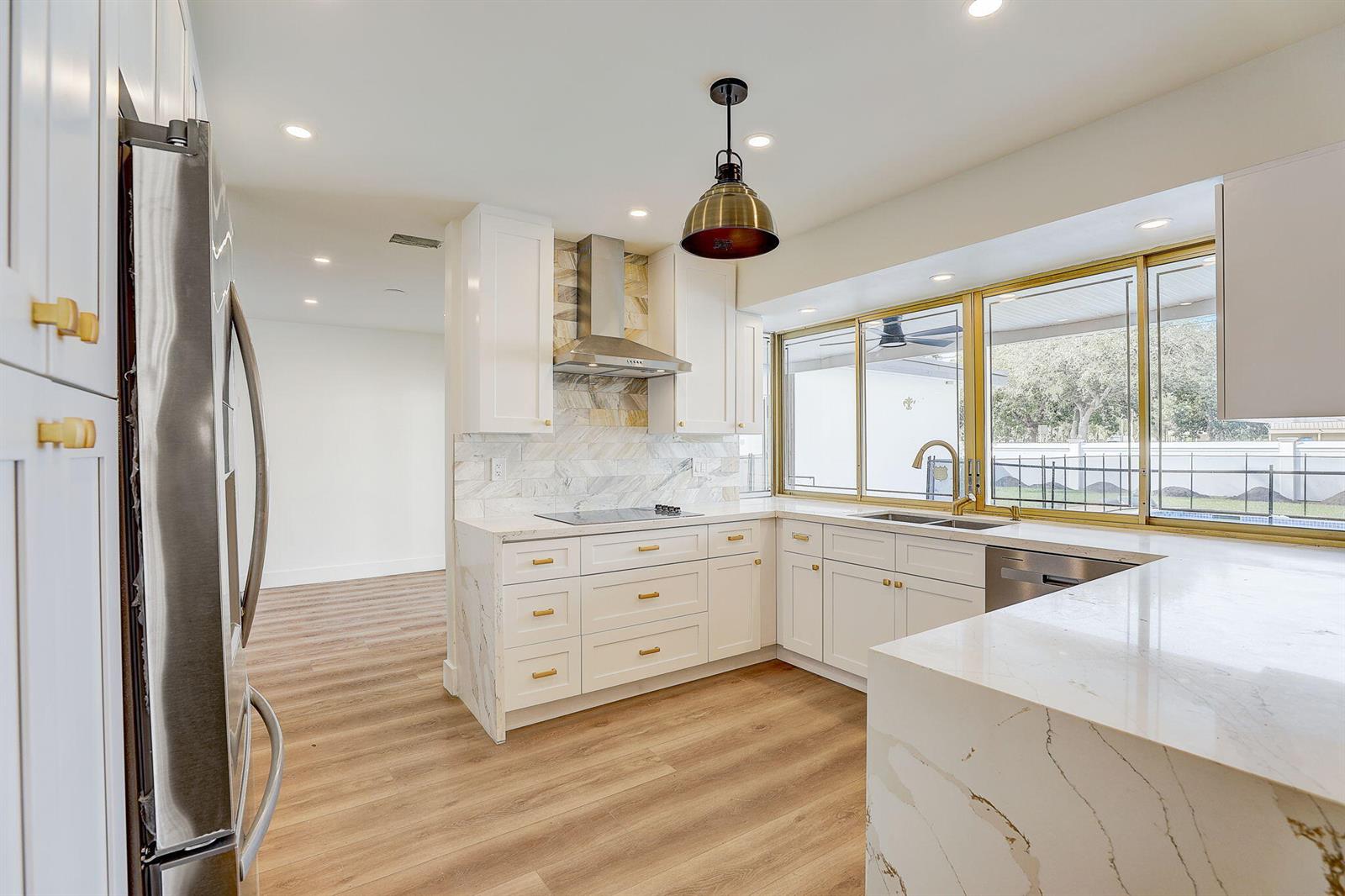 A modern kitchen features white cabinetry, marble countertops, gold hardware, and a large window — 3900 N 45th Avenue, Hollywood FL 33021, HOLLYWOOD, FL