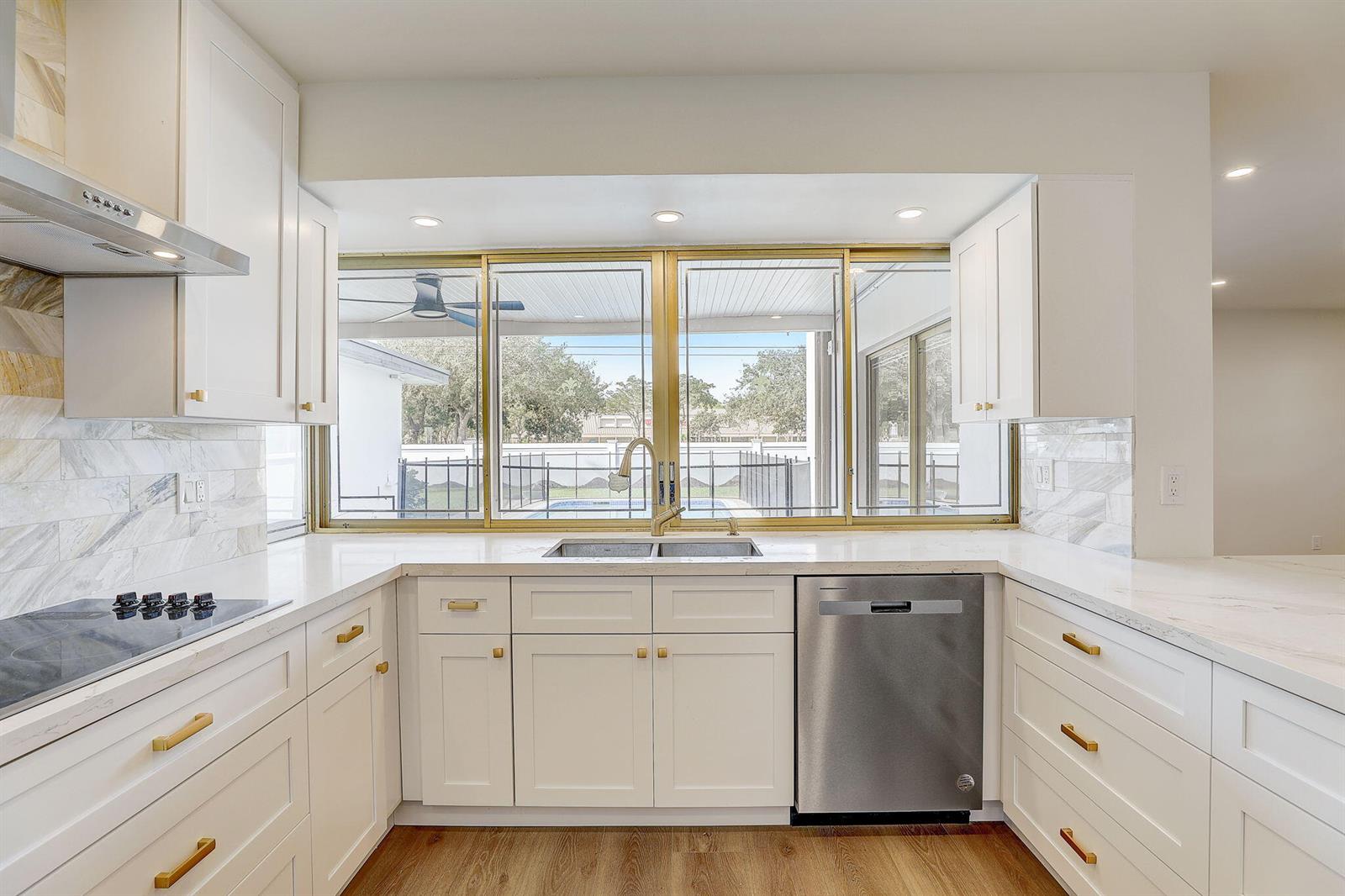 A white kitchen features gold hardware, marble-style backsplash, stainless steel appliances, and a window view — 3900 N 45th Avenue, Hollywood FL 33021, HOLLYWOOD, FL