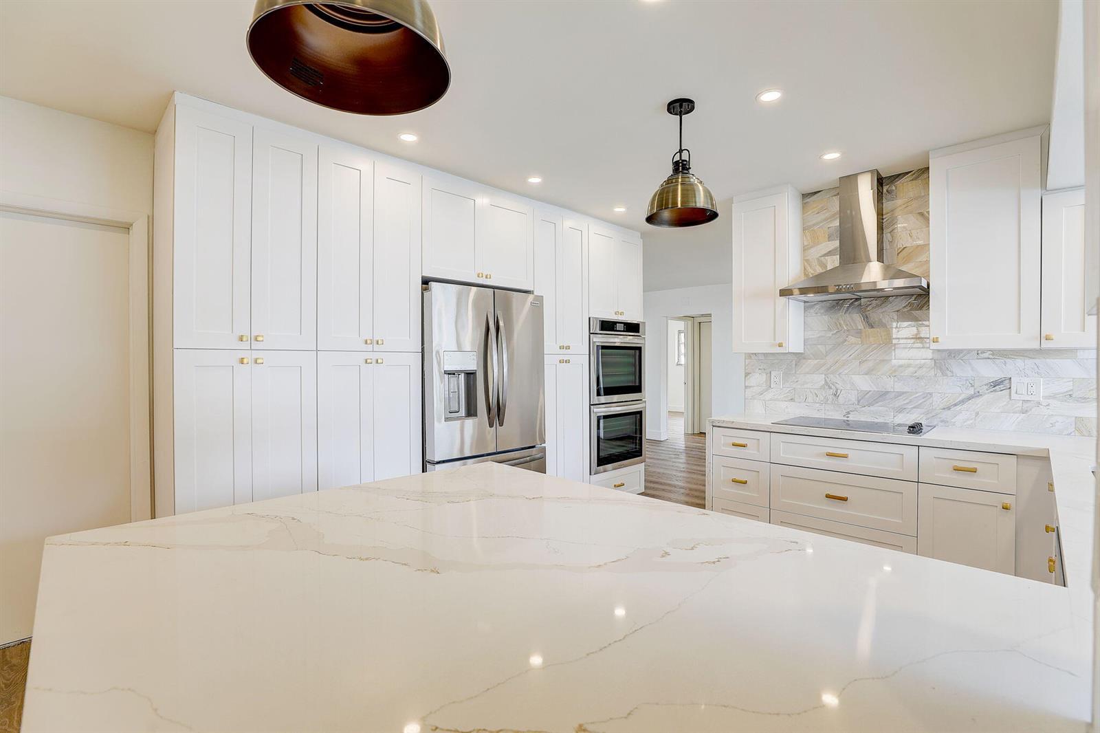A modern kitchen features white cabinetry, stainless steel appliances, and a large marble-topped island — 3900 N 45th Avenue, Hollywood FL 33021, HOLLYWOOD, FL