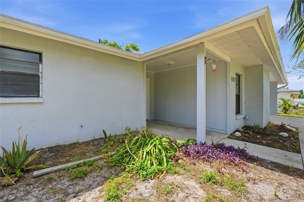 A light-colored house exterior features a covered entryway, a concrete walkway, and a landscaped yard — 1163 RINGTAIL ROAD, VENICE, FL
