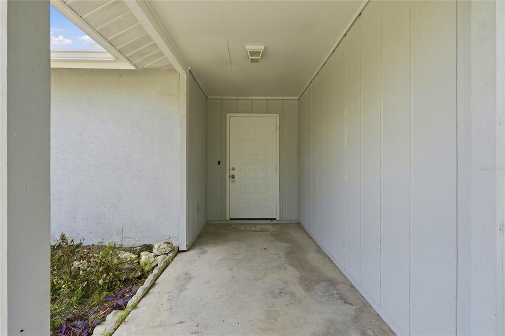 A covered entryway features a white paneled door, light gray siding, and a concrete floor — 1163 RINGTAIL ROAD, VENICE, FL