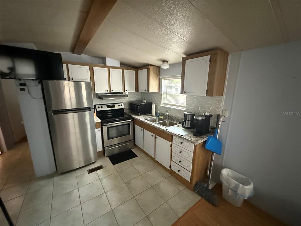 A kitchen features stainless steel appliances, white cabinets, tiled flooring, and a window above the sink — 3000 CLARCONA ROAD UNIT 2715, APOPKA, FL