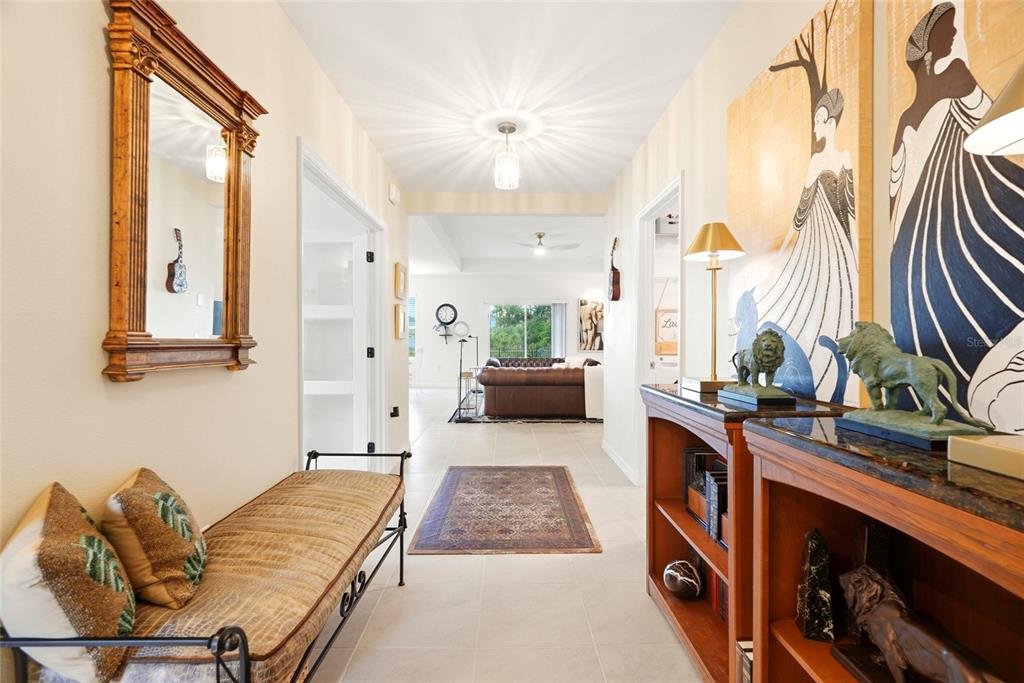 A hallway features a bench, a console table with lion statues, and artwork leading toward a living room — 9860 LAST LIGHT GLEN, PARRISH, FL