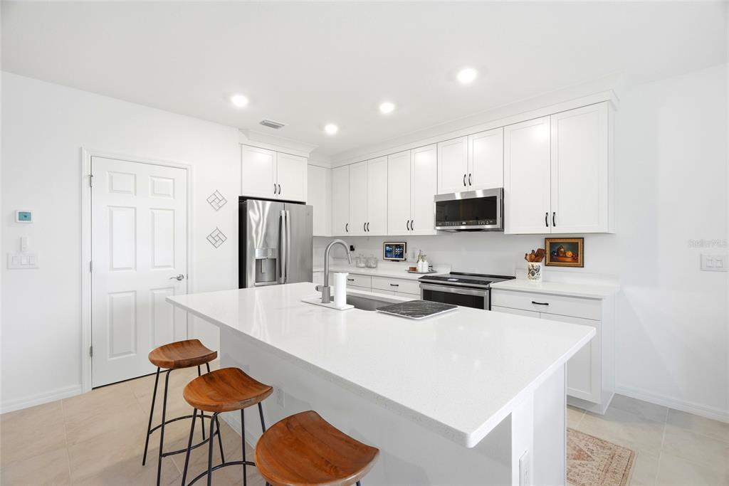 A modern kitchen features white cabinetry, a large quartz island, and three wooden bar stools — 9860 LAST LIGHT GLEN, PARRISH, FL