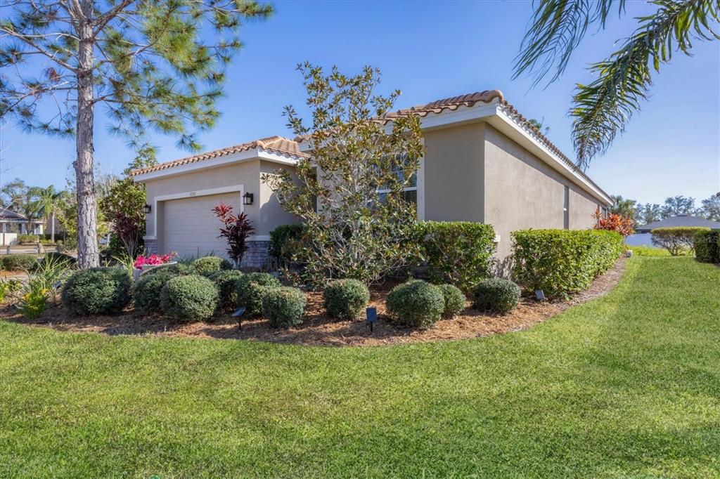 A tan single-story house with a tile roof, a two-car garage, and landscaped front yard — 5333 CHARLIE BROWN LANE, SARASOTA, FL