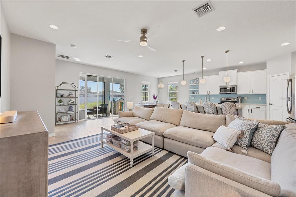 A spacious open-concept living room features a large sectional sofa, striped rug, and kitchen area — 5333 CHARLIE BROWN LANE, SARASOTA, FL