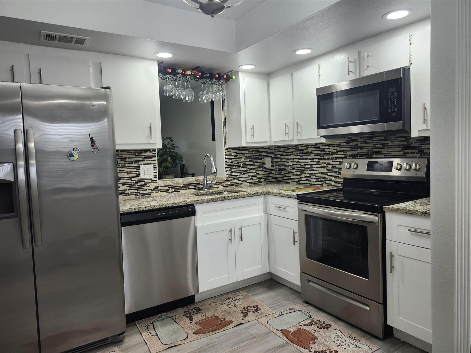 A kitchen features white cabinets, stainless steel appliances, granite countertops, and a mosaic tile backsplash — 7684 NW 18th Street # 101, Margate FL 33063, MARGATE, FL