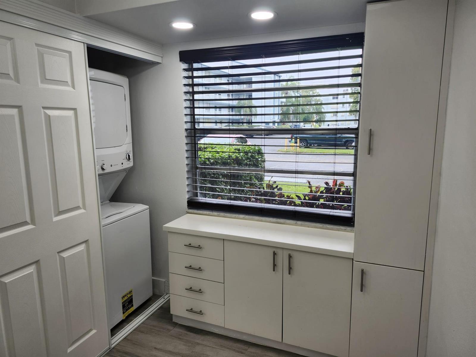 A laundry room featuring a stacked washer-dryer, white cabinetry, and a window with dark blinds — 7684 NW 18th Street # 101, Margate FL 33063, MARGATE, FL
