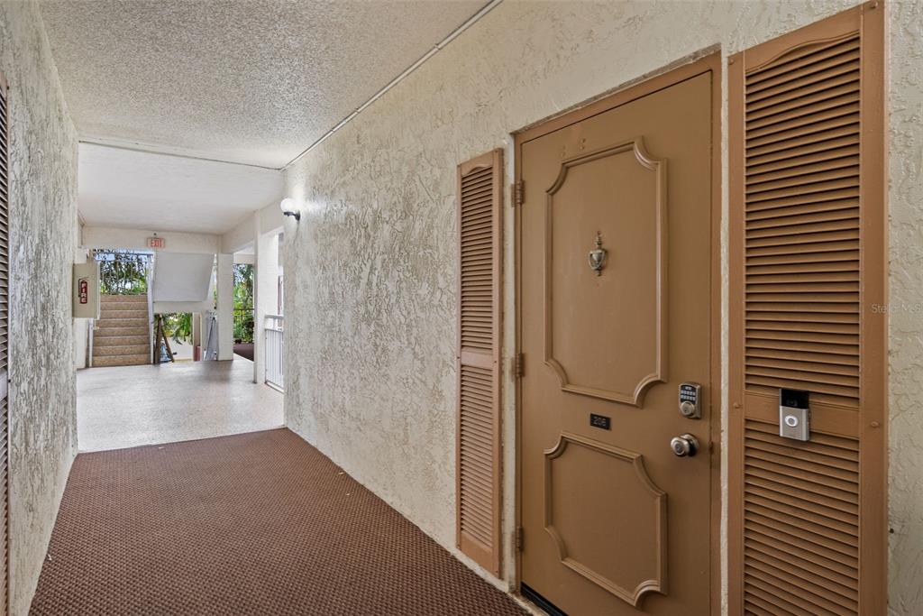 A brown front door with a smart lock and shutters sits along a covered walkway — 1860 MASSACHUSETTS AVENUE NE UNIT 206, ST PETERSBURG, FL