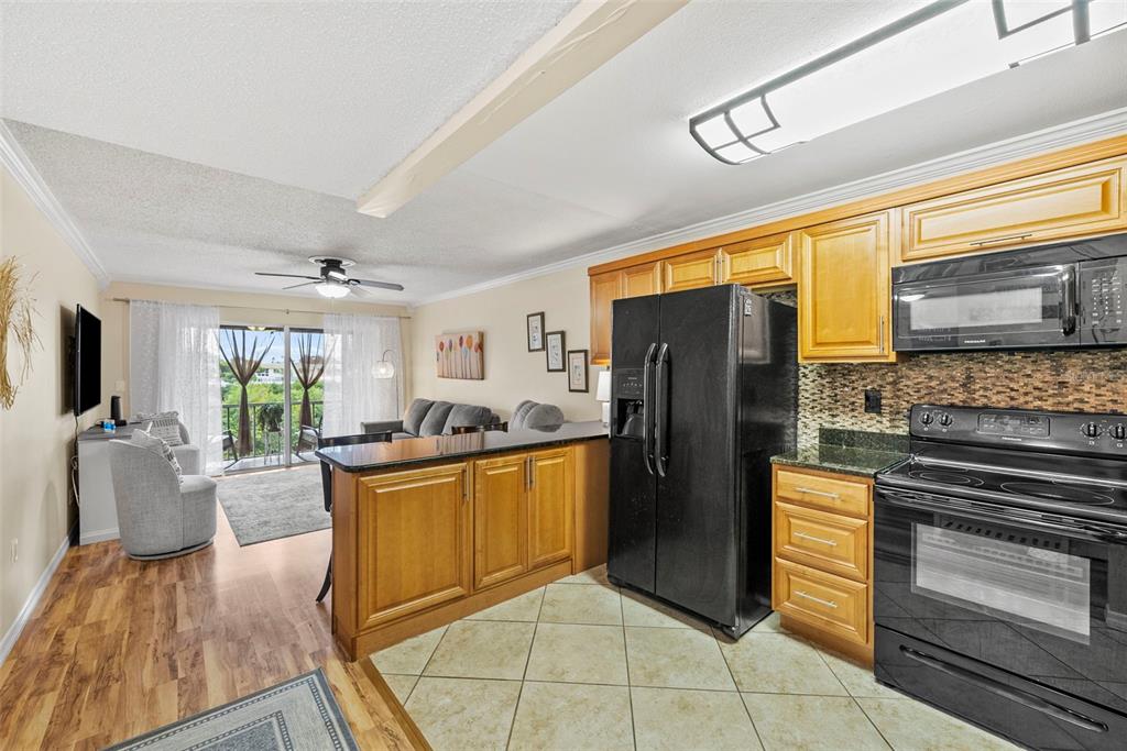 A kitchen with wood cabinets and black appliances opens into a living area with balcony access — 1860 MASSACHUSETTS AVENUE NE UNIT 206, ST PETERSBURG, FL