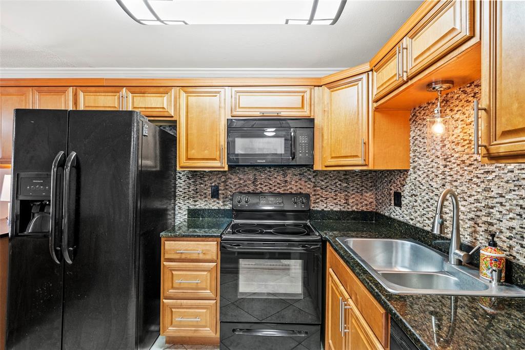A kitchen features wood cabinets, black appliances, dark granite countertops, and a mosaic tile backsplash — 1860 MASSACHUSETTS AVENUE NE UNIT 206, ST PETERSBURG, FL