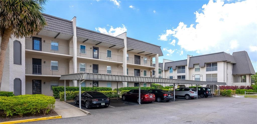 A multi-story apartment building features a covered parking area with several cars parked underneath — 8703 BARDMOOR BOULEVARD UNIT 305, SEMINOLE, FL