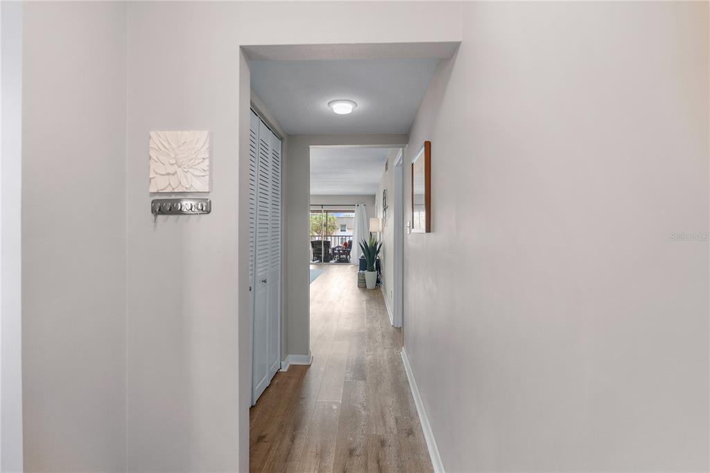 A hallway with light wood-look flooring leads toward a living area with a balcony view — 8703 BARDMOOR BOULEVARD UNIT 305, SEMINOLE, FL
