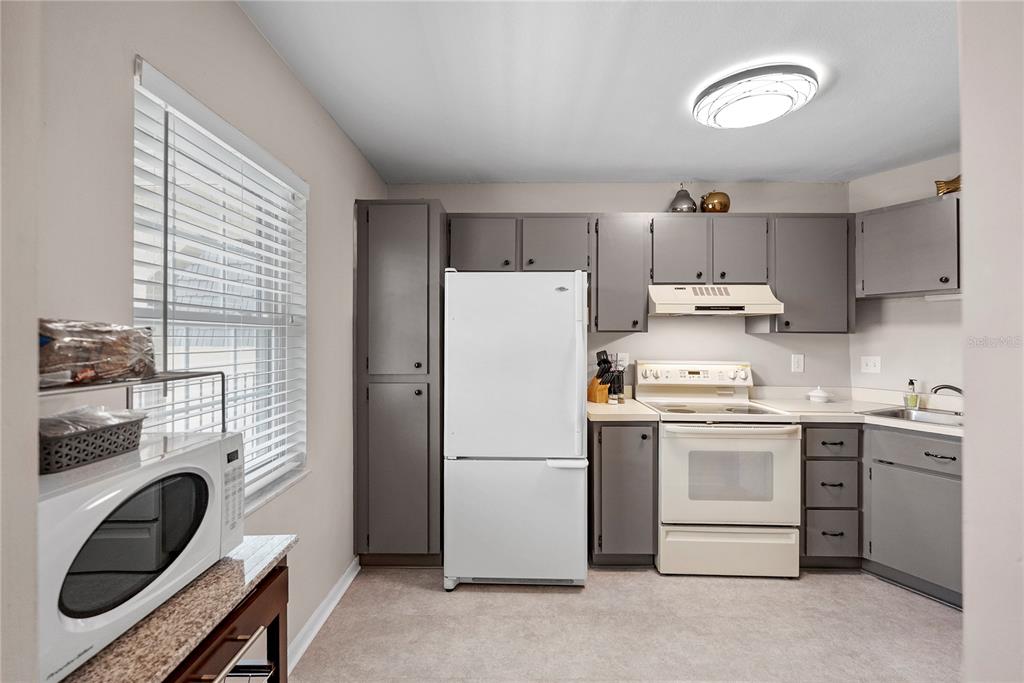 A kitchen features gray cabinets, white appliances, a window with blinds, and a microwave — 8703 BARDMOOR BOULEVARD UNIT 305, SEMINOLE, FL