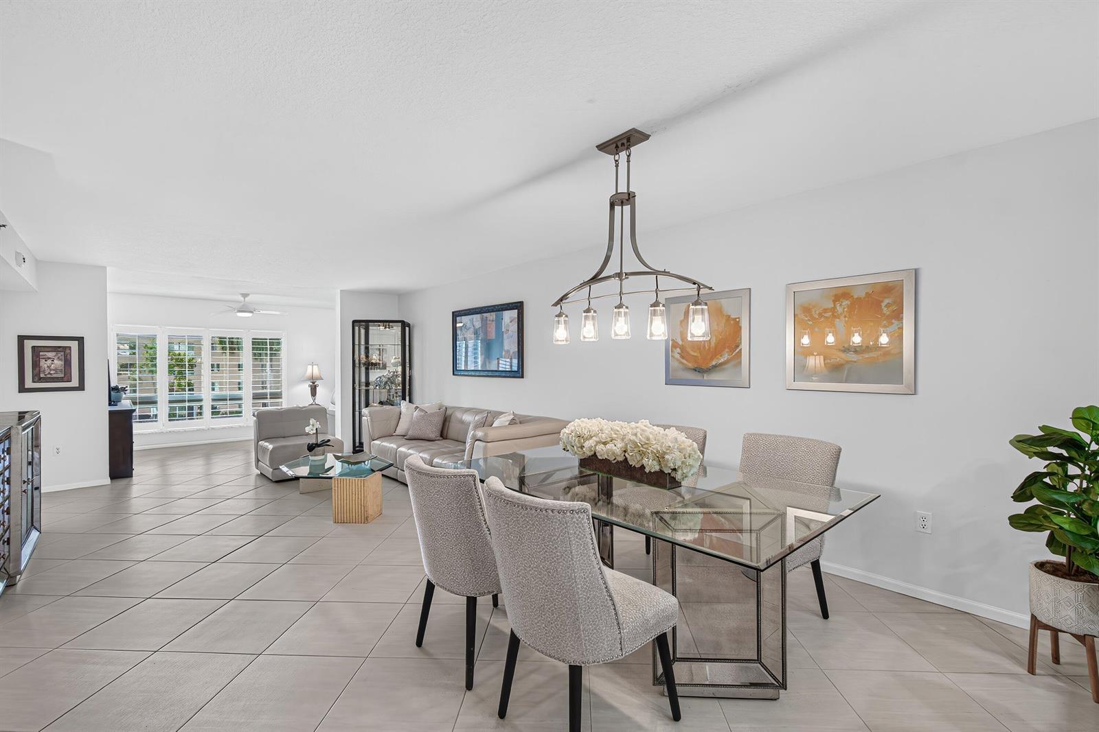A dining area with a glass table and chandelier opens into a living room with tile floors — 12540 Majesty Circle # 303, Boynton Beach FL 33437, BOYNTON BEACH, FL