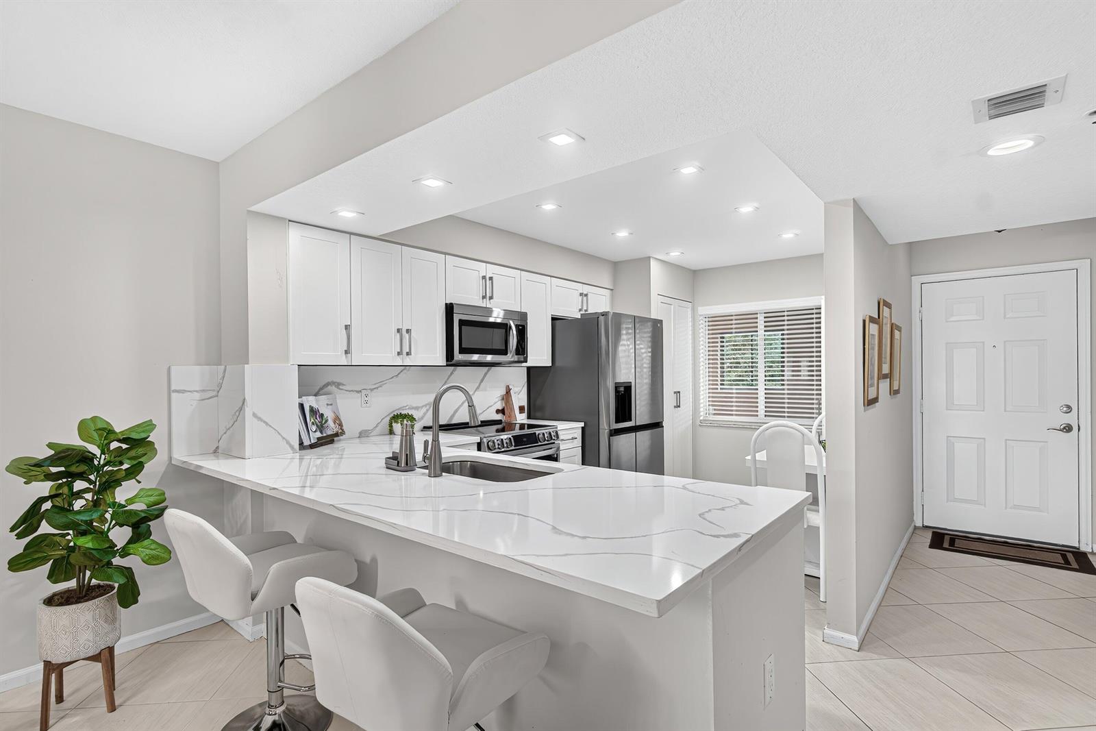 A modern kitchen features white cabinets, marble-patterned countertops, stainless steel appliances, and a breakfast bar — 12540 Majesty Circle # 303, Boynton Beach FL 33437, BOYNTON BEACH, FL
