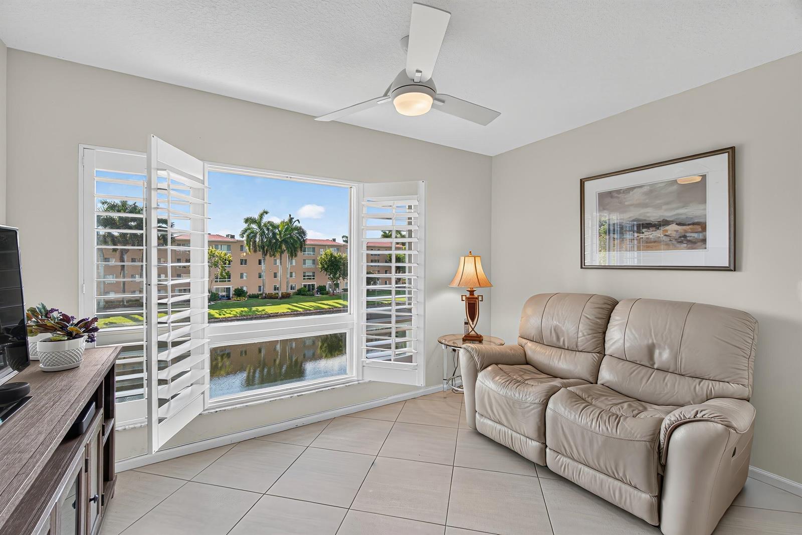 A living room features a beige leather sofa, tile flooring, and a window overlooking water — 12540 Majesty Circle # 303, Boynton Beach FL 33437, BOYNTON BEACH, FL