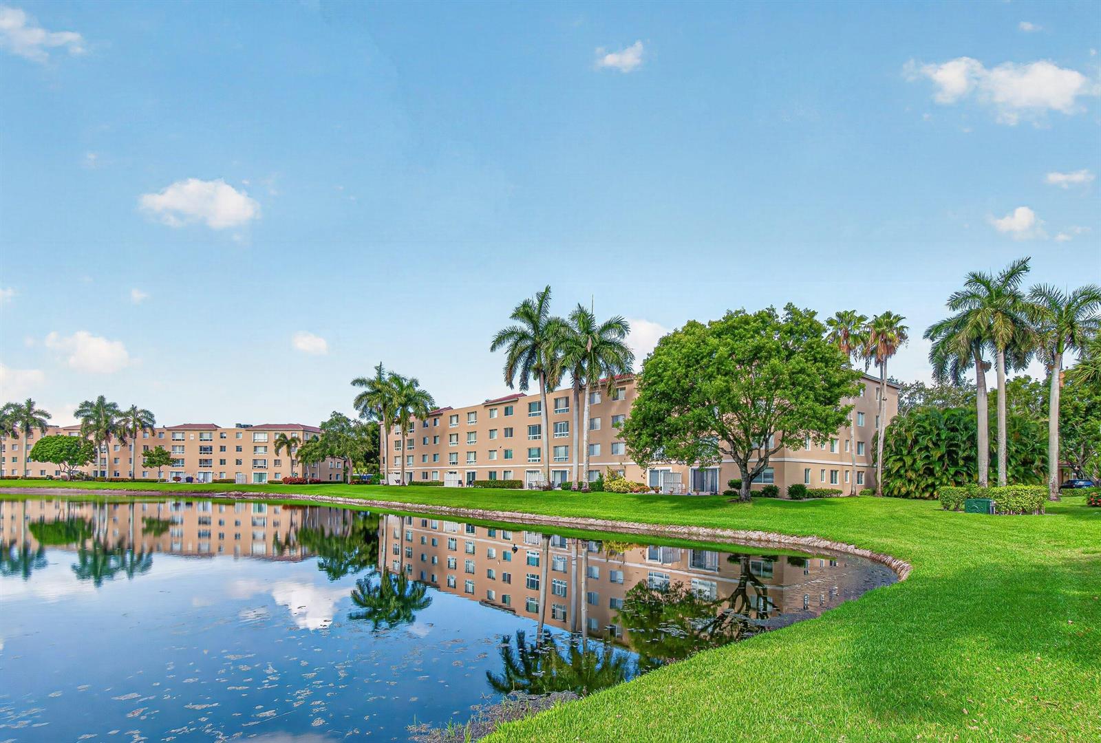 A multi-story apartment building sits beside a lake surrounded by palm trees and green grass — 12540 Majesty Circle # 303, Boynton Beach FL 33437, BOYNTON BEACH, FL