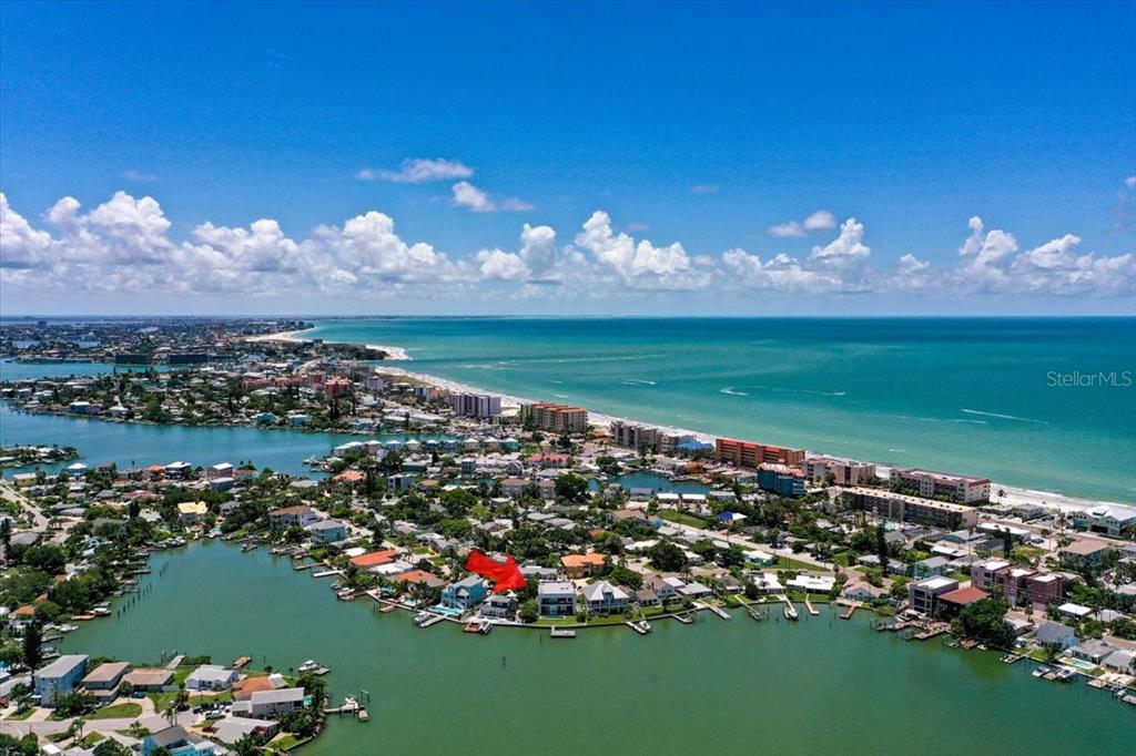 An aerial view shows a waterfront house with a red arrow pointing to it — 14077 N BAYSHORE DRIVE, MADEIRA BEACH, FL