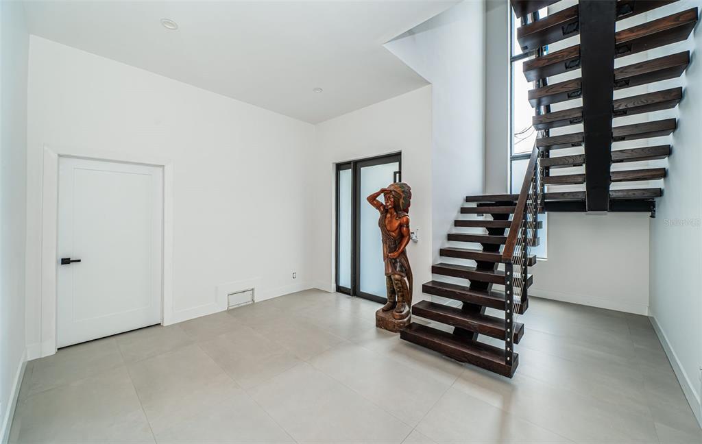 A modern entryway features large gray floor tiles, a wooden statue, and a floating staircase — 14077 N BAYSHORE DRIVE, MADEIRA BEACH, FL