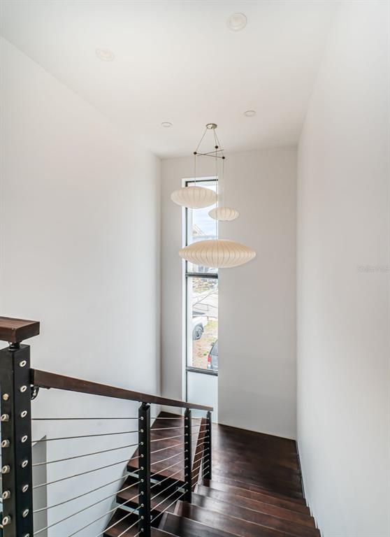 A modern staircase with dark wood treads and a cable railing features a tiered pendant light — 14077 N BAYSHORE DRIVE, MADEIRA BEACH, FL