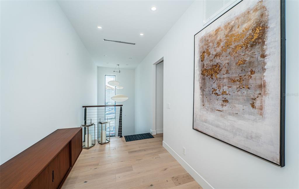 A modern hallway features light wood flooring, a large abstract painting, and a staircase railing — 14077 N BAYSHORE DRIVE, MADEIRA BEACH, FL