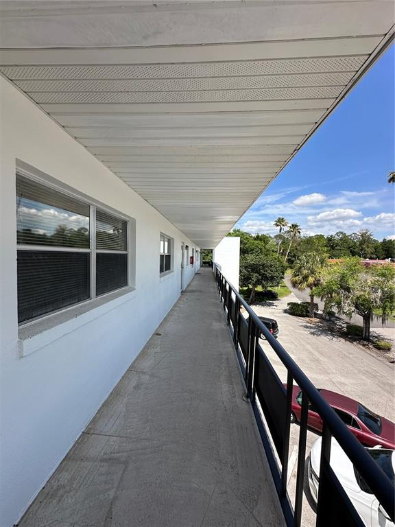 An outdoor walkway with a metal railing overlooks a parking lot and trees — 100 EL CAMINO DRIVE UNIT 309, WINTER HAVEN, FL