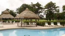 A swimming pool sits in front of two thatched-roof gazebos and lounge chairs on a patio — 6100 NW 44th St # 405, Lauderhill FL 33319, LAUDERHILL, FL