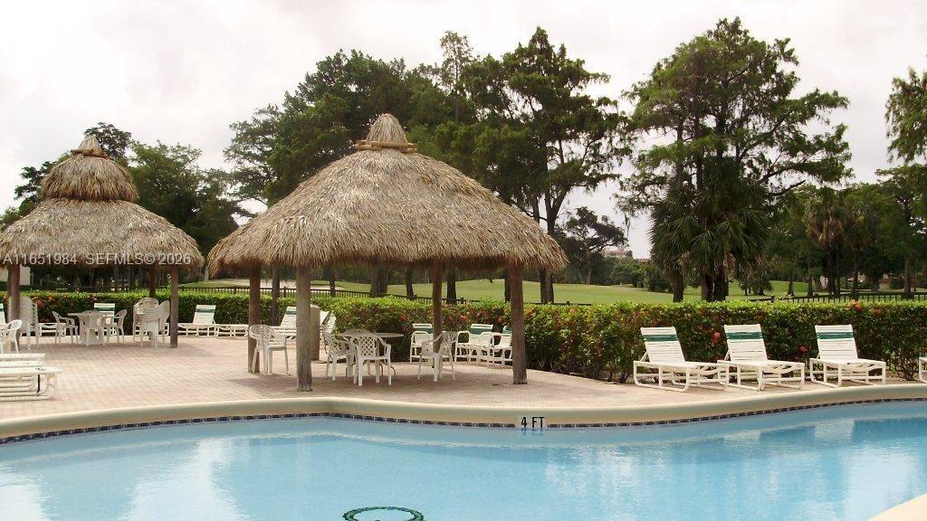 A swimming pool sits in front of two thatched-roof gazebos and lounge chairs — 6100 NW 44th St # 405, Lauderhill FL 33319, LAUDERHILL, FL