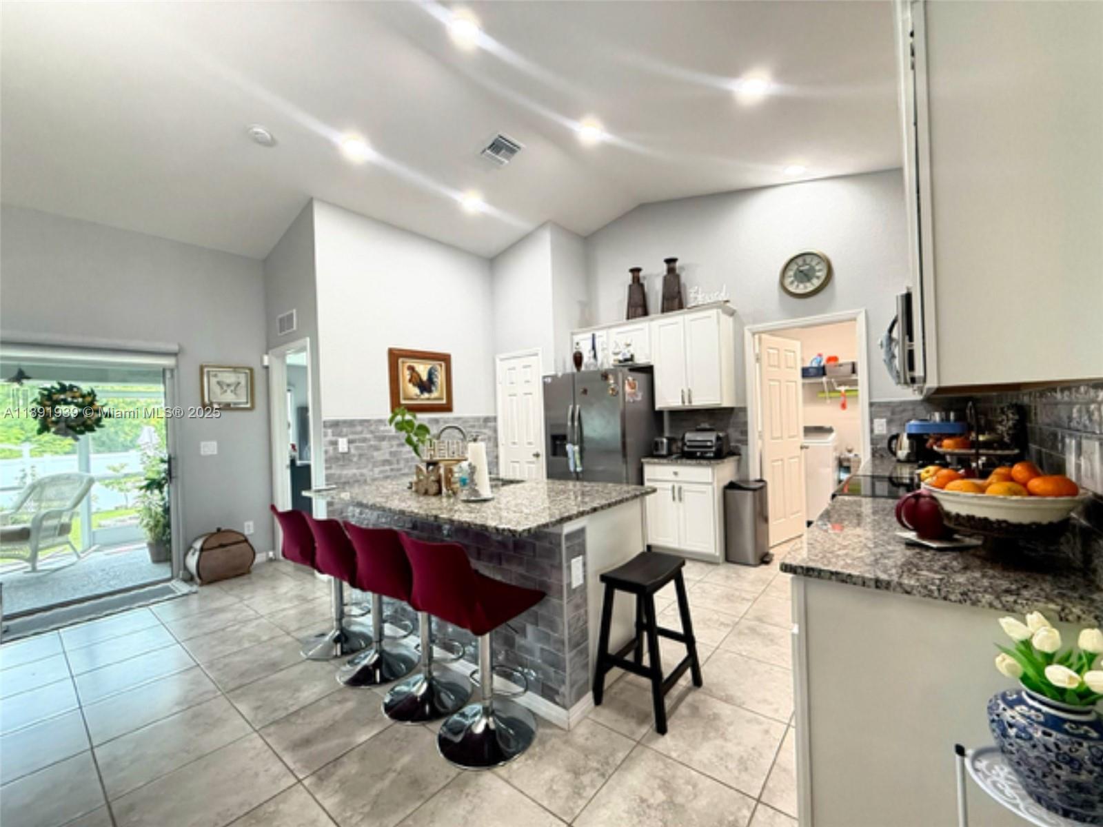 A kitchen features a granite-topped island with red bar stools and light tile flooring — 4157 NW 40th ave, Cape Coral FL 33993, CAPE CORAL, FL