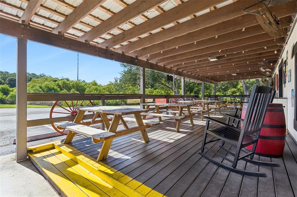 A covered wooden deck features picnic tables, a rocking chair, and a red barrel — 36721 COUNTY ROAD 19A, EUSTIS, FL