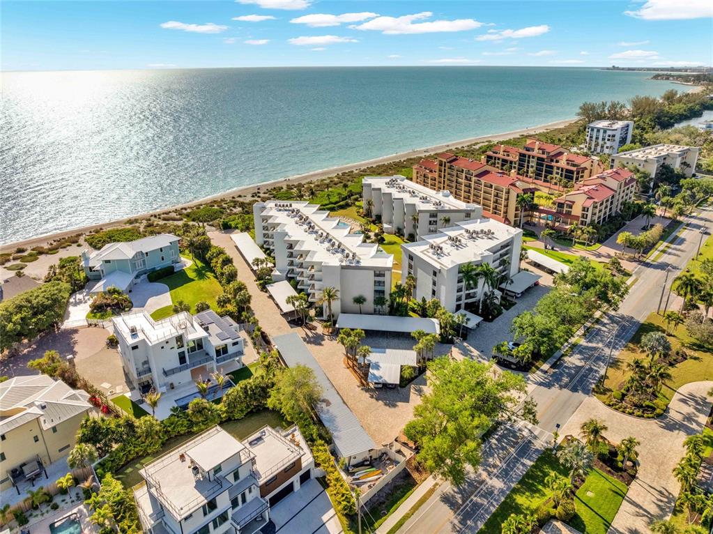 An aerial view shows a multi-story beachfront condominium complex with a pool and parking area — 8764 MIDNIGHT PASS ROAD UNIT A201, SARASOTA, FL