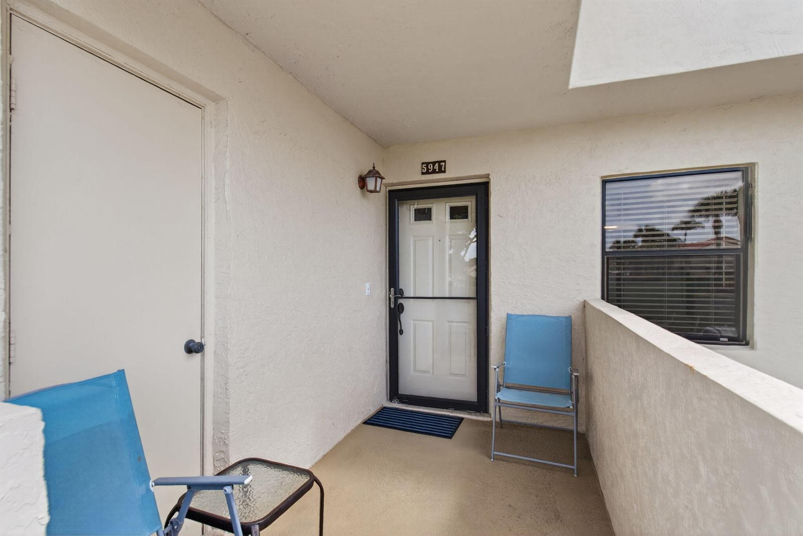 An outdoor balcony features a white door, a screen door, and two blue folding chairs — 5947 Parkwalk Drive, Boynton Beach FL 33472, BOYNTON BEACH, FL
