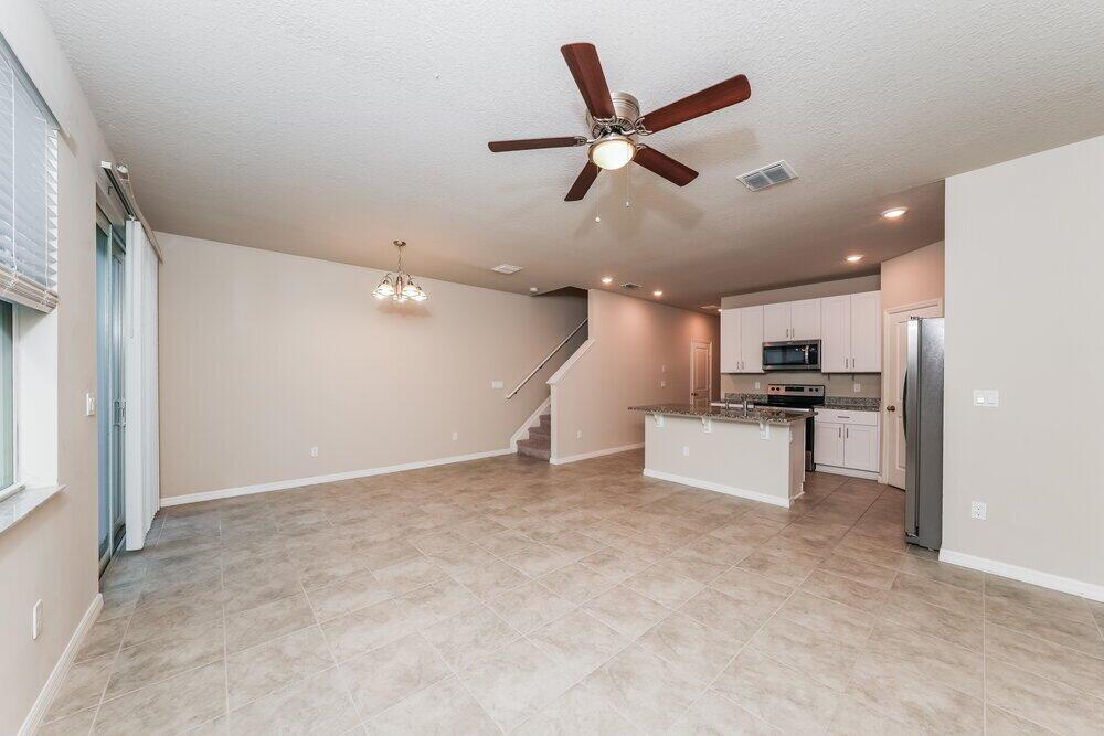 An open-concept living and dining area features tile flooring, a kitchen island, and a staircase — PALM SPRINGS, FL