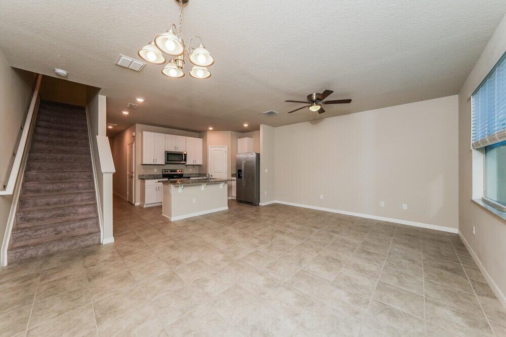 An open-concept living area with tile flooring, a kitchen with white cabinets, and carpeted stairs — PALM SPRINGS, FL