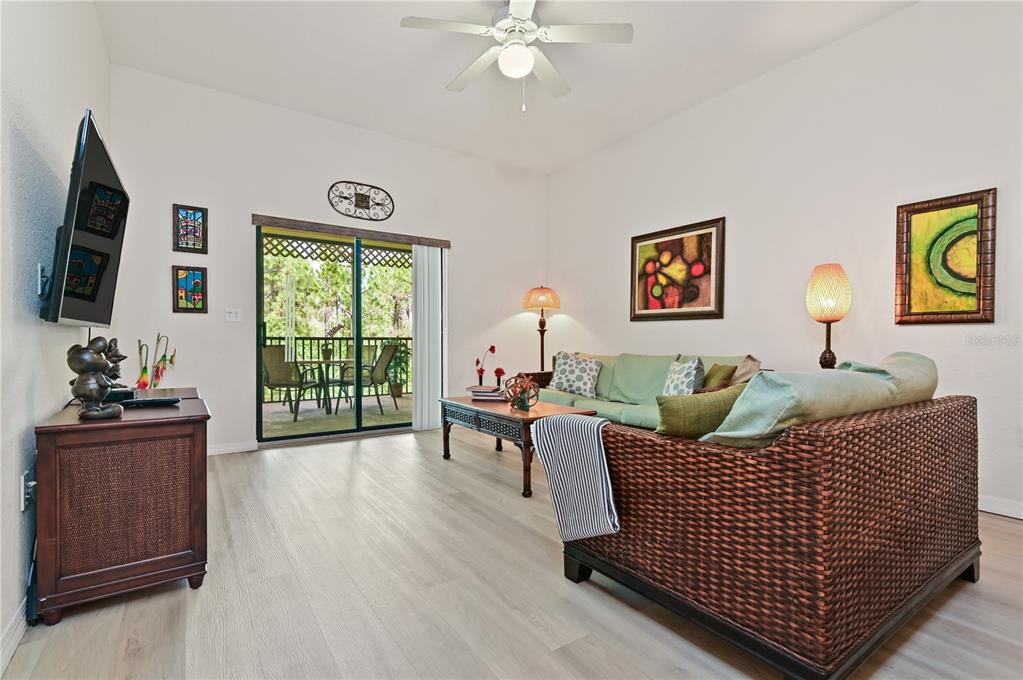 A living room features a wicker sofa, light wood flooring, and a sliding glass door — 3060 PIRATES RETREAT COURT UNIT 302, KISSIMMEE, FL