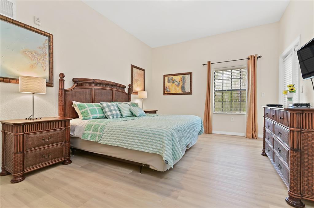 A bedroom features a king-sized bed, wicker furniture, light wood-look flooring, and a window — 3060 PIRATES RETREAT COURT UNIT 302, KISSIMMEE, FL