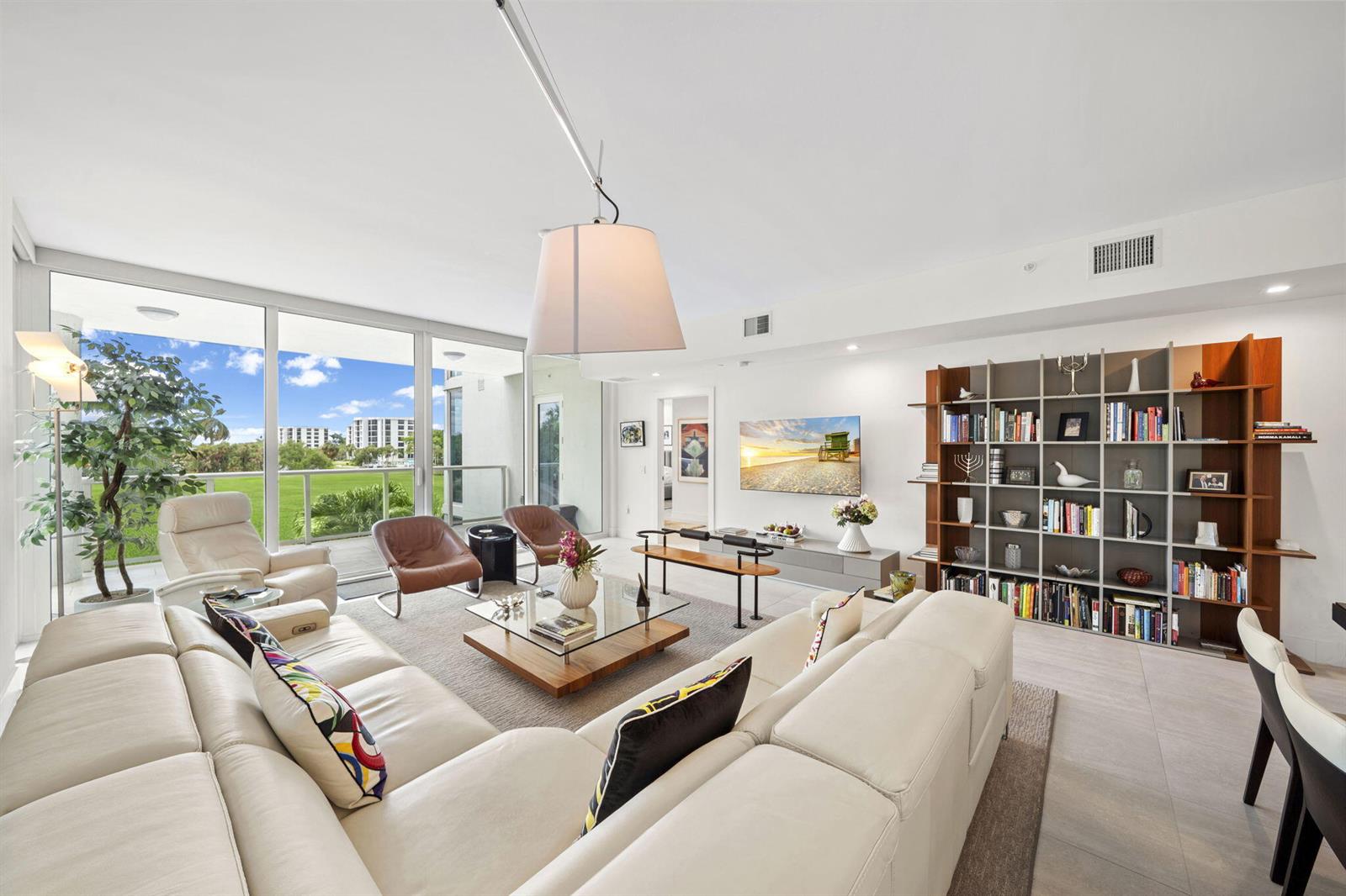 A modern living room features a white sectional sofa, glass coffee table, and large bookshelf — 20155 Boca West Drive # C201, Boca Raton FL 33434, BOCA RATON, FL