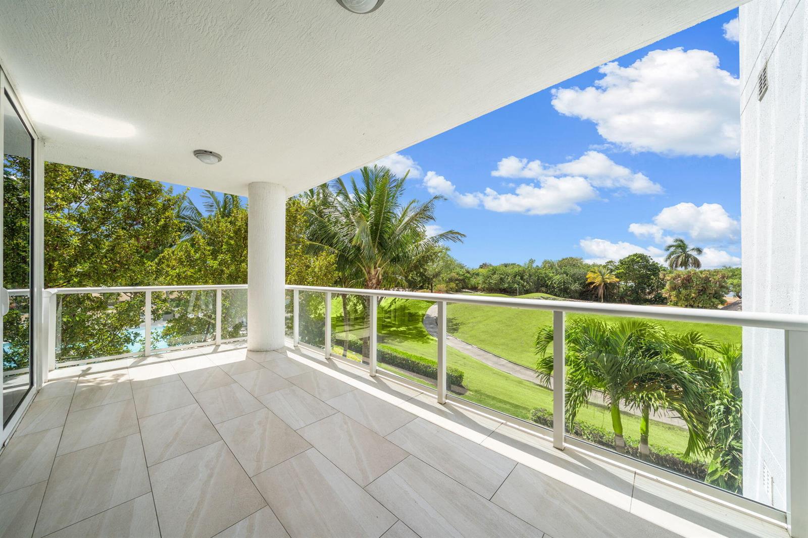 A tiled balcony with a glass railing overlooks a grassy golf course and palm trees — 20155 Boca West Drive # C201, Boca Raton FL 33434, BOCA RATON, FL