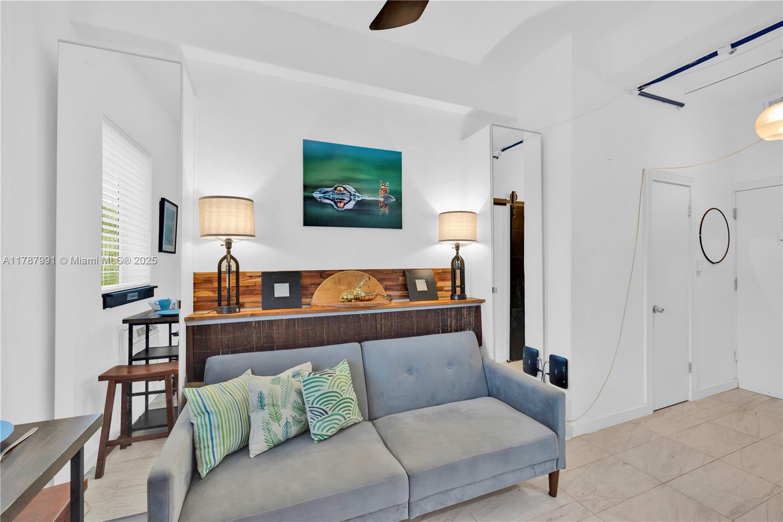 A living room features a gray sofa, two lamps, and a wall-mounted alligator artwork — 255 W 24th St # 136, Miami Beach FL 33140, MIAMI BEACH, FL