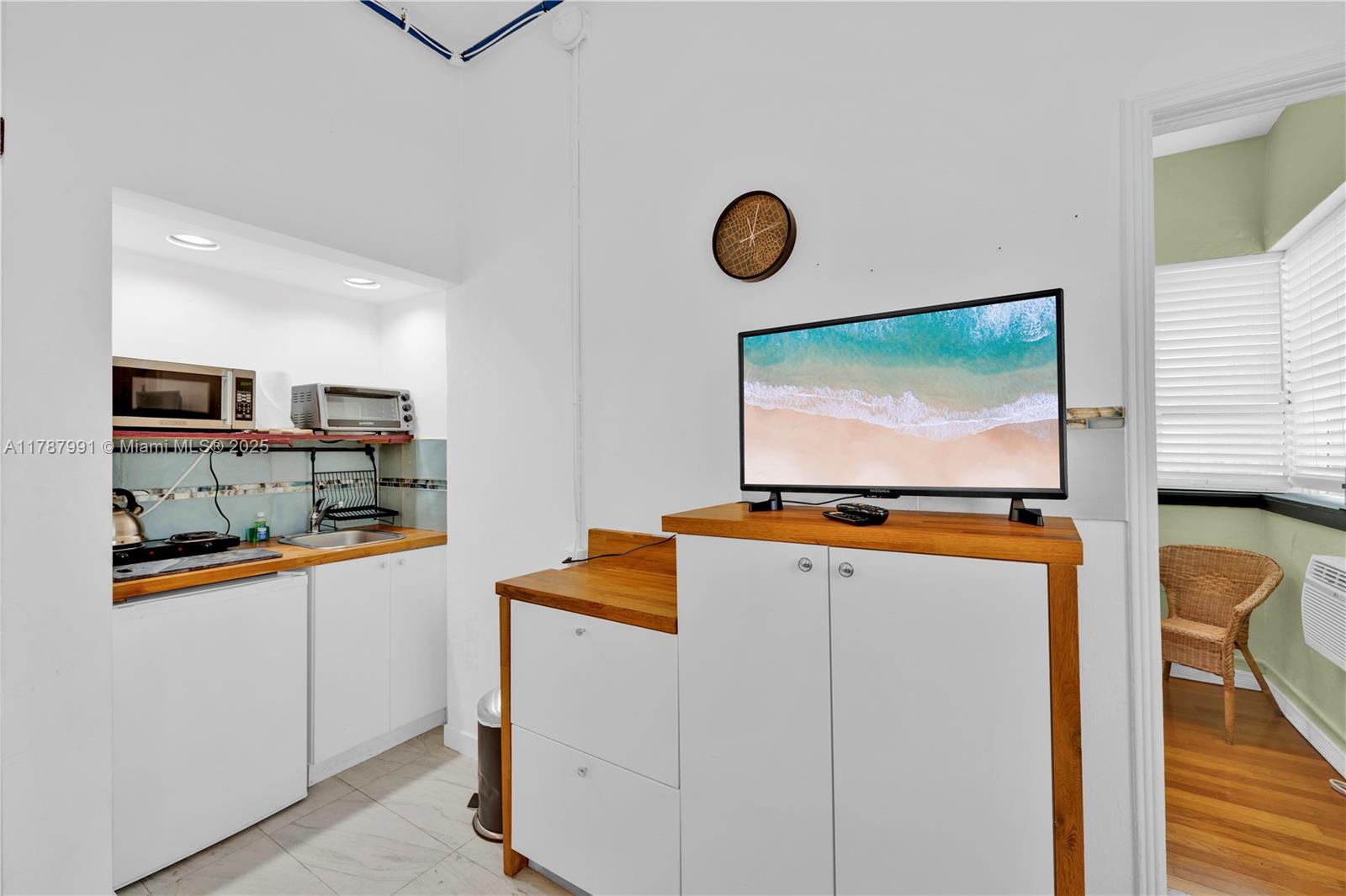 This small kitchen area features white cabinets, wood countertops, and a television on a console — 255 W 24th St # 136, Miami Beach FL 33140, MIAMI BEACH, FL