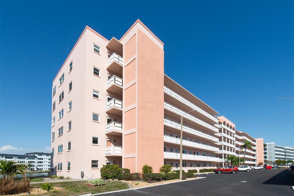 A multi-story, light pink apartment building with exterior walkways and balconies under a clear sky — 6025 SHORE BOULEVARD S UNIT 405, GULFPORT, FL