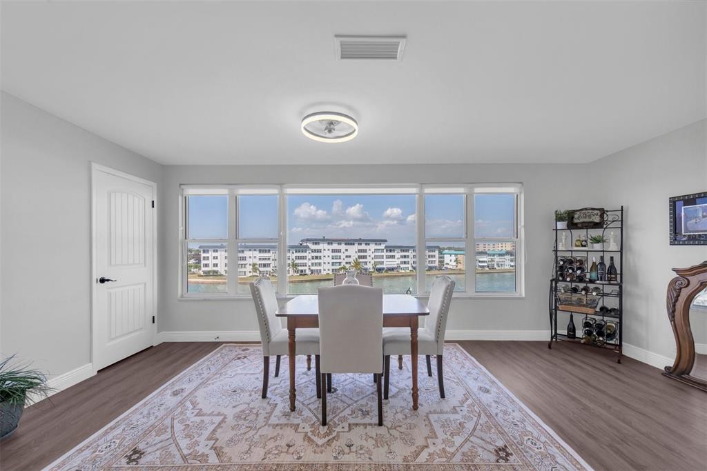 A dining room features a wooden table, four upholstered chairs, a rug, and waterfront views — 6025 SHORE BOULEVARD S UNIT 405, GULFPORT, FL