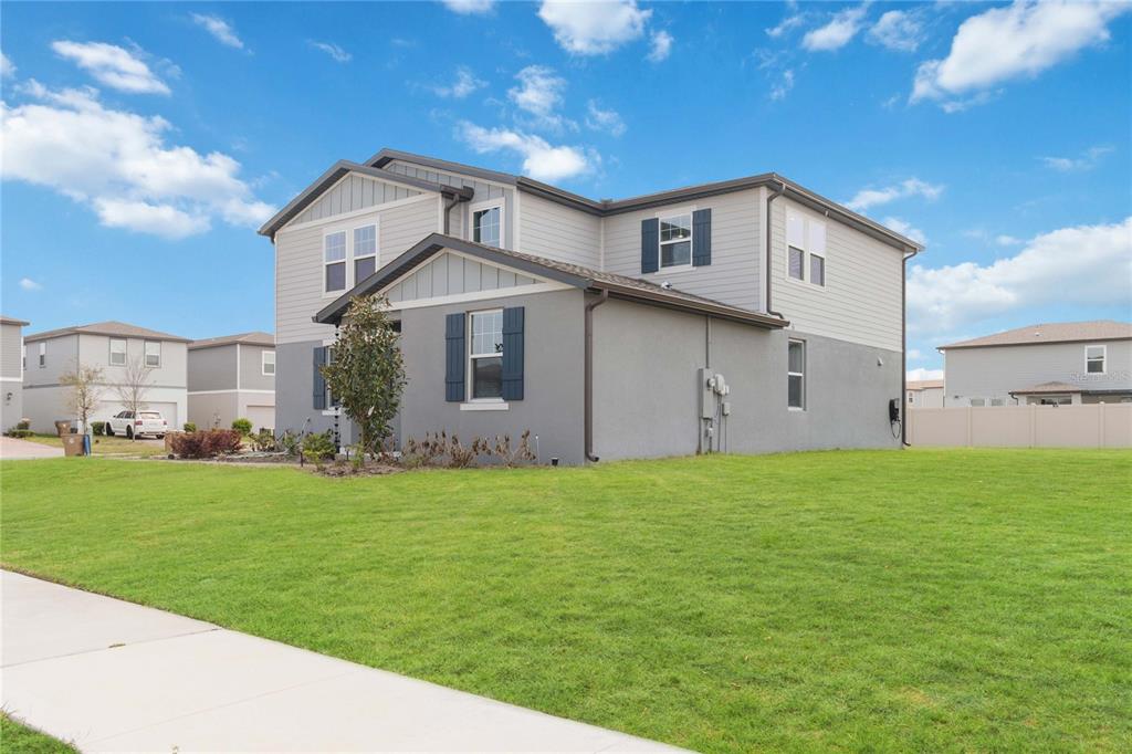 A two-story house with gray siding and stucco exterior sits on a large grass lawn — 5298 MEREDREW LANE, ST CLOUD, FL