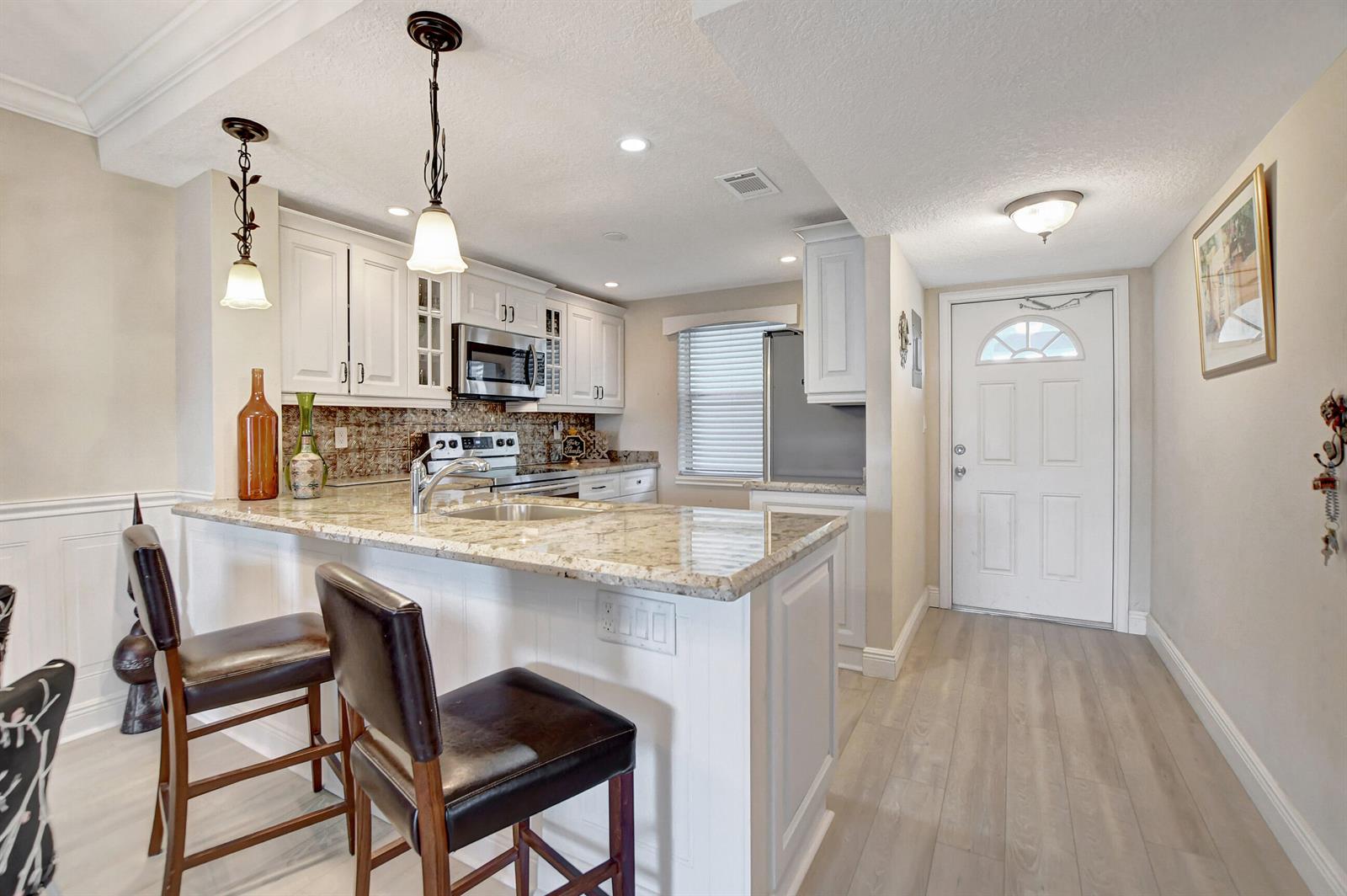 A kitchen with white cabinets, stainless steel appliances, granite countertops, and a metallic patterned backsplash — 9810 Marina Boulevard # 1120, Boca Raton FL 33428, BOCA RATON, FL
