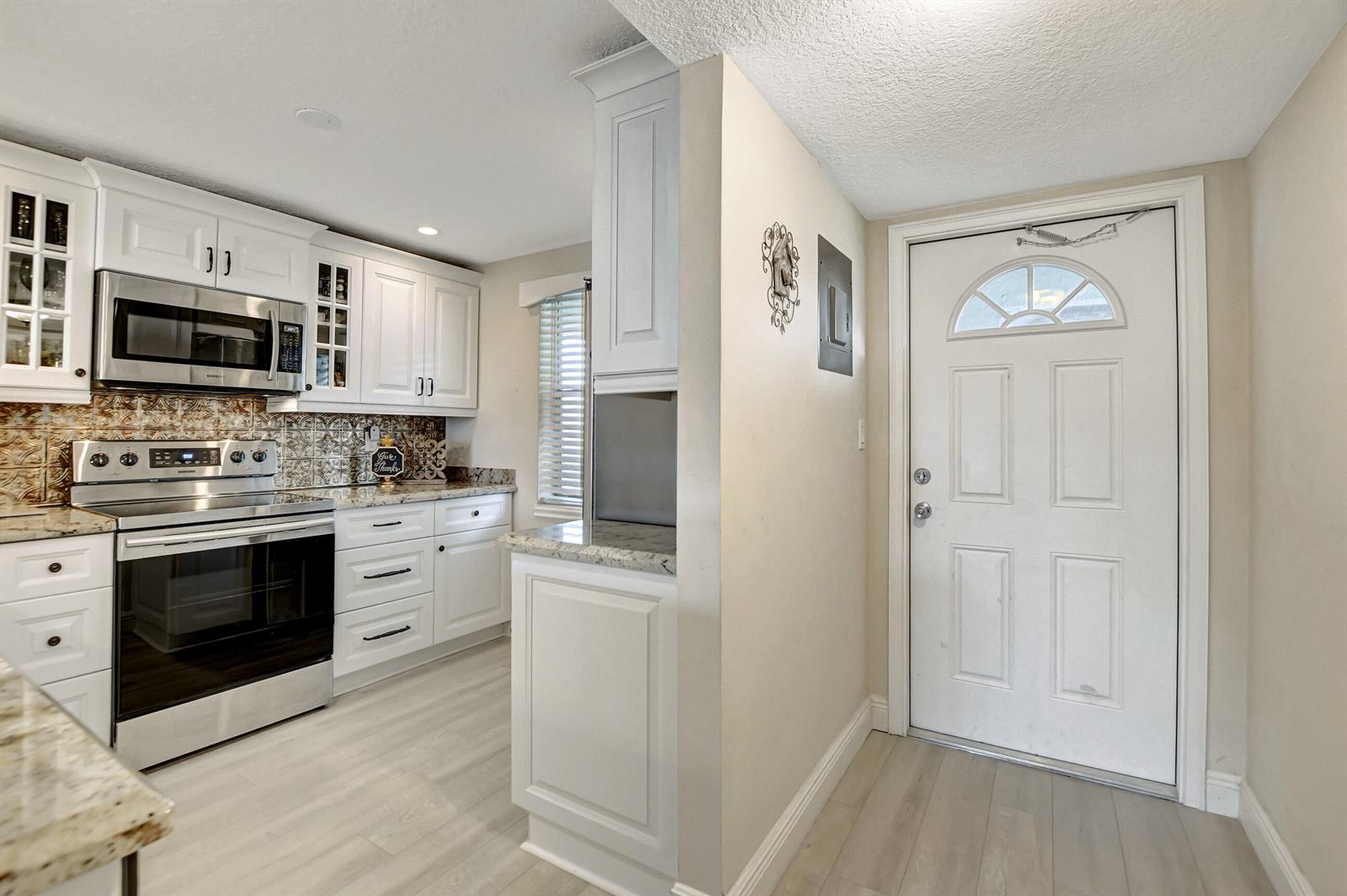A kitchen features white cabinetry, granite countertops, a breakfast bar with stools, and light flooring — 9810 Marina Boulevard # 1120, Boca Raton FL 33428, BOCA RATON, FL