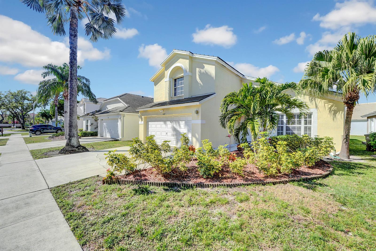 A yellow two-story house with a garage and palm trees sits on a suburban street — 2008 Normandy Circle, West Palm Beach FL 33409, WEST PALM BEACH, FL