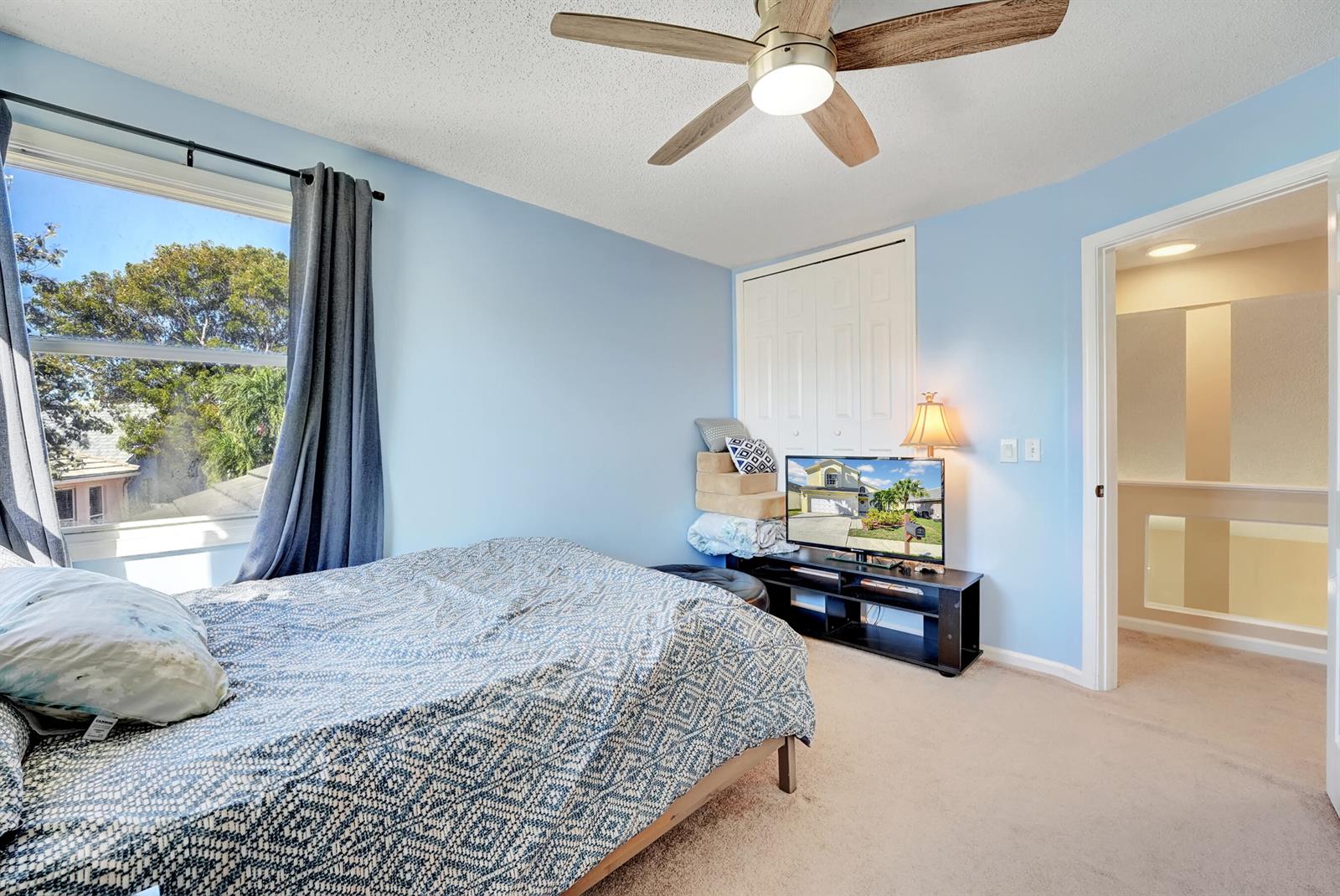 A bedroom features light blue walls, a ceiling fan, a bed, and a television stand — 2008 Normandy Circle, West Palm Beach FL 33409, WEST PALM BEACH, FL