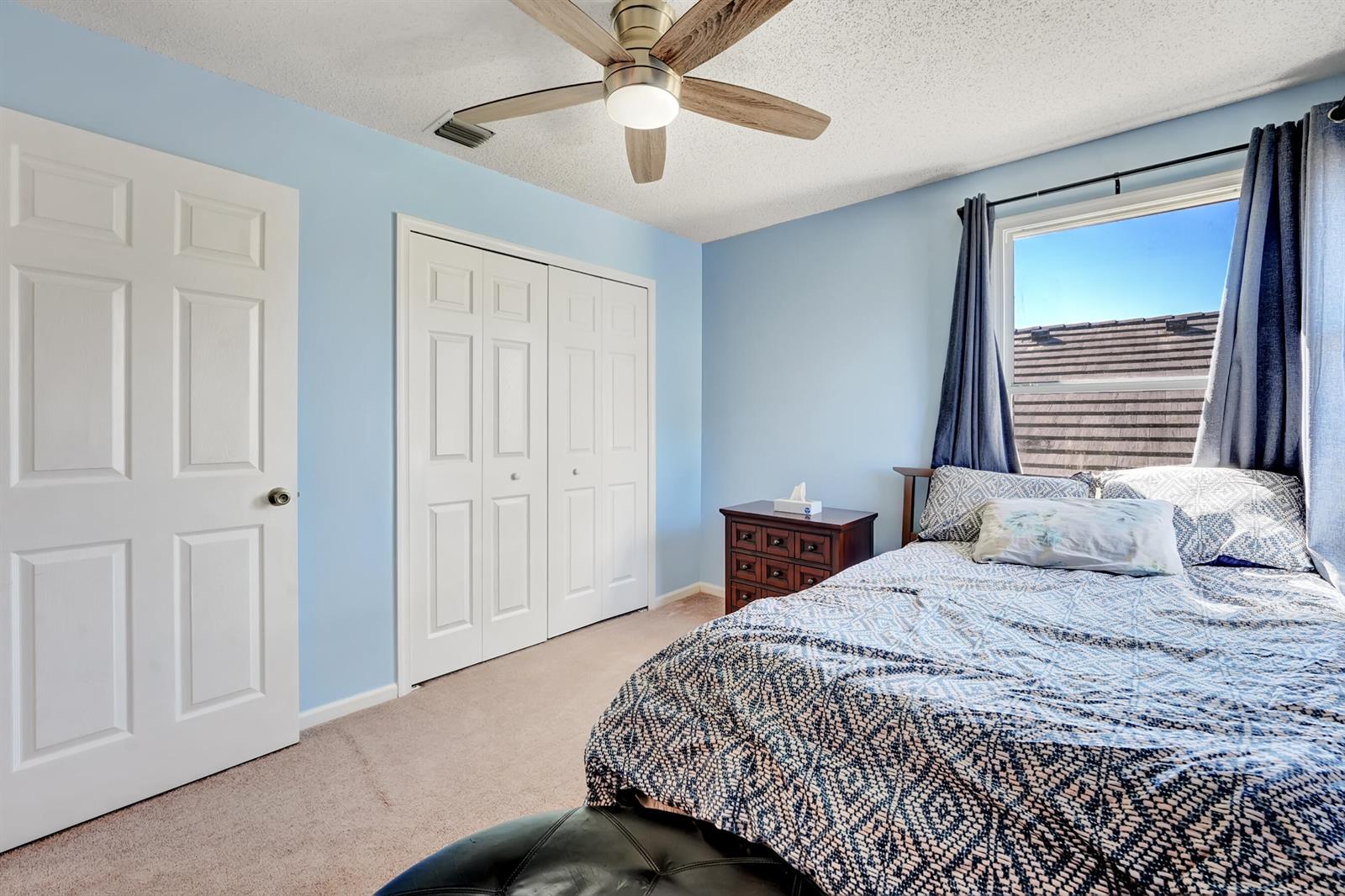 A bedroom with light blue walls, a ceiling fan, a bed, and white closet doors — 2008 Normandy Circle, West Palm Beach FL 33409, WEST PALM BEACH, FL